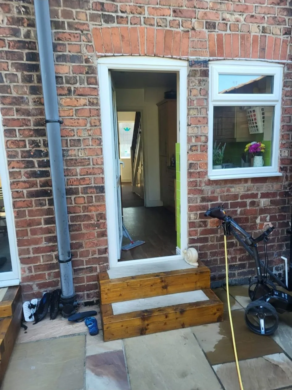 New white external door in a red brick wall with matched brickwork around the opening and timber steps below
